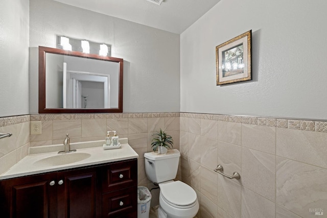 bathroom featuring wainscoting, tile walls, vanity, and toilet