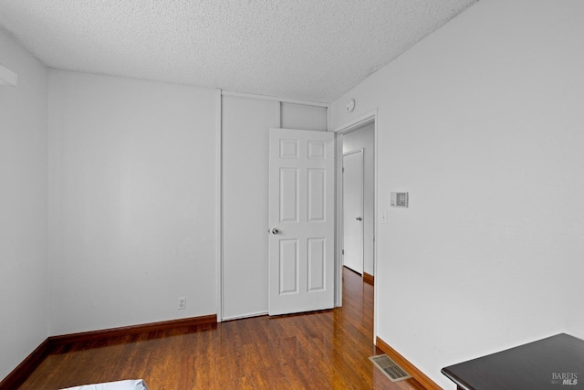 empty room featuring baseboards, a textured ceiling, visible vents, and wood finished floors