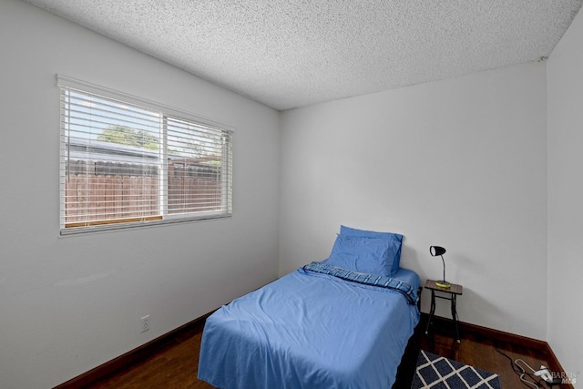 bedroom featuring a textured ceiling, baseboards, and wood finished floors