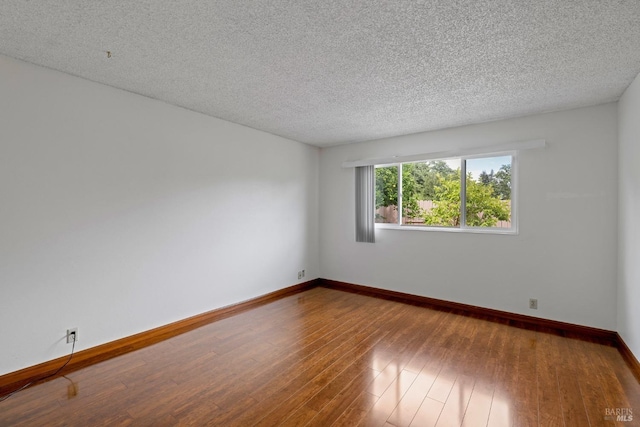 empty room with baseboards, wood-type flooring, and a textured ceiling