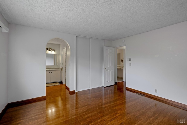 unfurnished bedroom featuring visible vents, wood finished floors, baseboards, a textured ceiling, and arched walkways