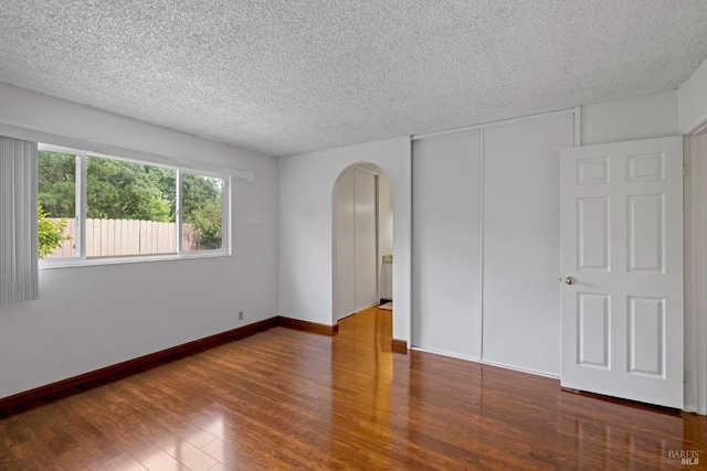 unfurnished room with baseboards, arched walkways, a textured ceiling, and wood finished floors