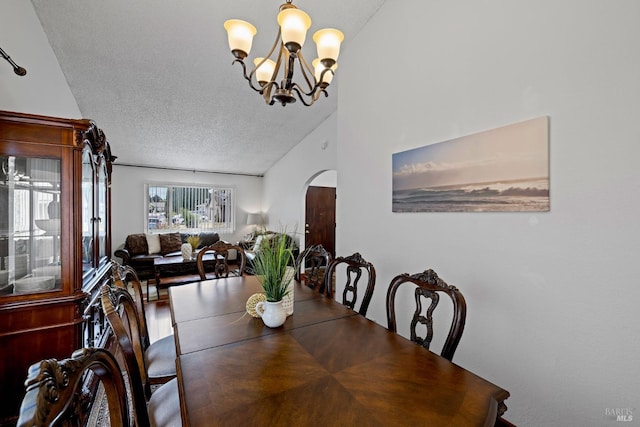 dining area featuring arched walkways, a textured ceiling, a notable chandelier, and vaulted ceiling