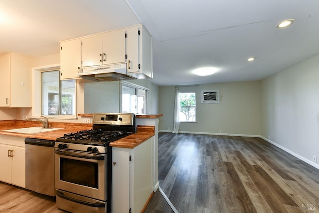 kitchen with a wall unit AC, sink, white cabinetry, dark wood-type flooring, and stainless steel appliances