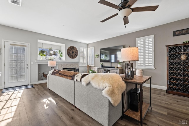 living room featuring a stone fireplace, ceiling fan, and dark wood-type flooring