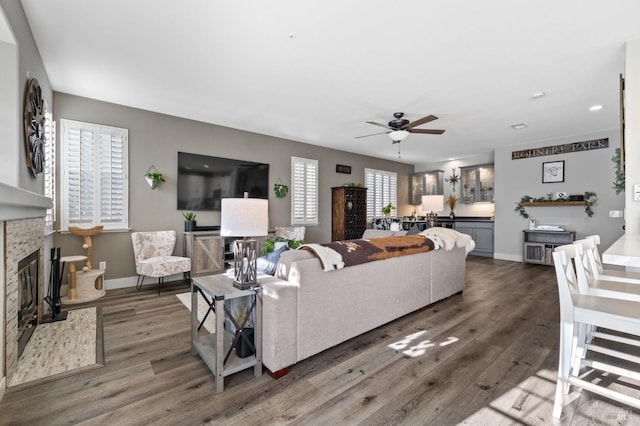 living room featuring plenty of natural light, ceiling fan, dark wood-type flooring, and a stone fireplace