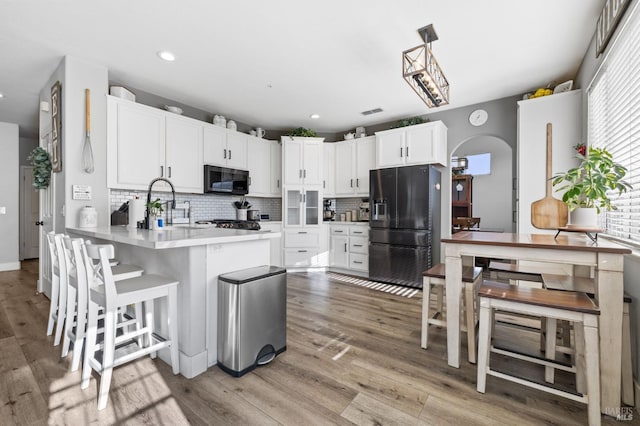 kitchen featuring white cabinets, hanging light fixtures, light wood-type flooring, black fridge with ice dispenser, and kitchen peninsula