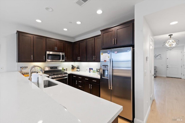 kitchen with dark brown cabinetry, stainless steel appliances, light countertops, and a sink