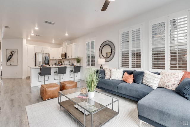 living room featuring light wood-type flooring, ceiling fan, and sink