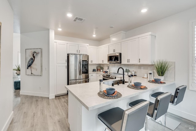 kitchen featuring a kitchen breakfast bar, kitchen peninsula, white cabinets, and appliances with stainless steel finishes