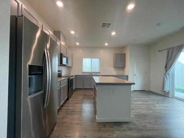 kitchen featuring hardwood / wood-style flooring, backsplash, appliances with stainless steel finishes, and a kitchen island