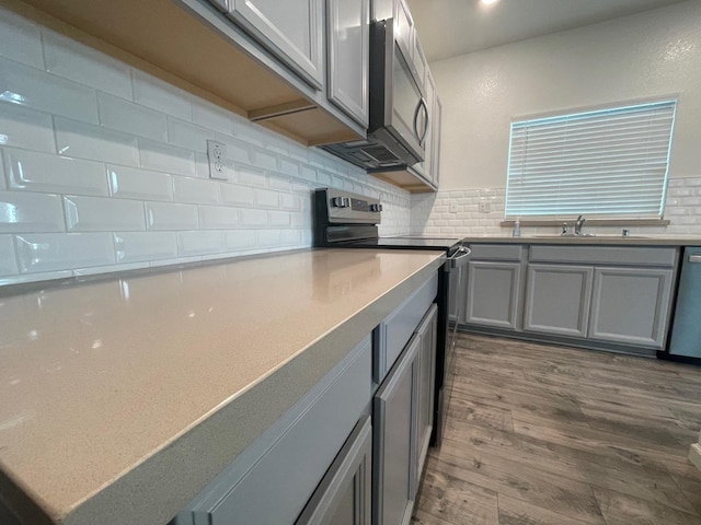 kitchen with gray cabinetry, sink, tasteful backsplash, wood-type flooring, and appliances with stainless steel finishes