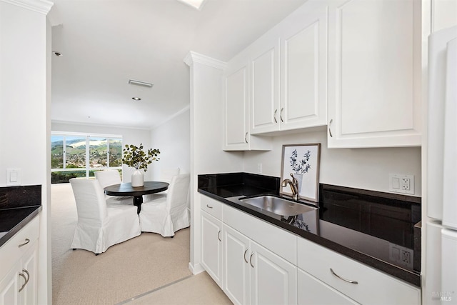 kitchen with white cabinetry, sink, light colored carpet, and ornamental molding