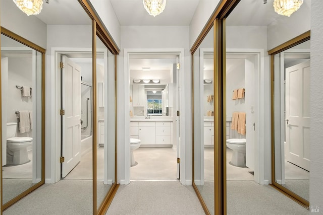 hall with light carpet, sink, and a notable chandelier