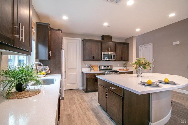 kitchen with dark brown cabinetry, stainless steel appliances, sink, a center island with sink, and light hardwood / wood-style flooring