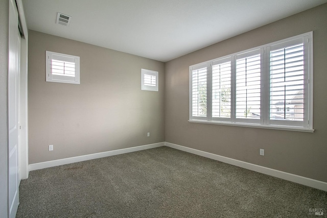 spare room with dark colored carpet and a wealth of natural light