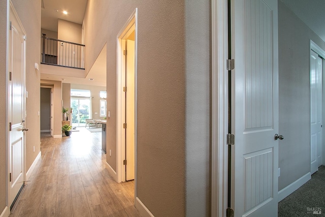 hall featuring a towering ceiling and light wood-type flooring