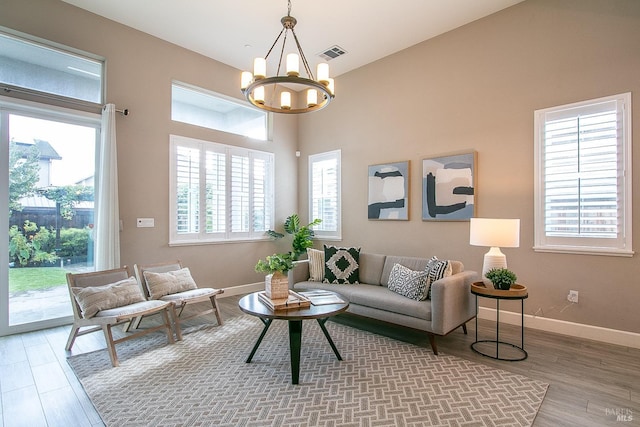 living room with a notable chandelier, wood-type flooring, and a towering ceiling