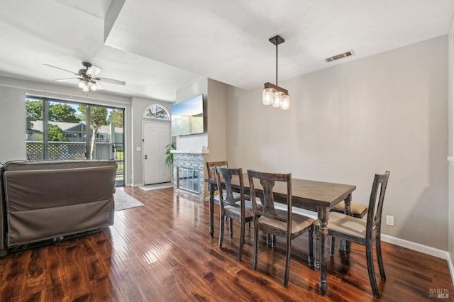 dining room with wood-type flooring, a stone fireplace, and ceiling fan with notable chandelier