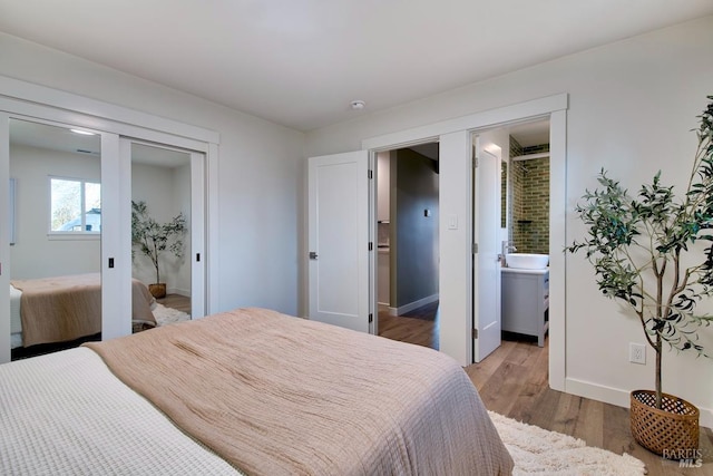 bedroom with connected bathroom, a closet, baseboards, and wood finished floors