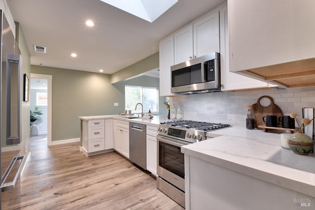 kitchen with white cabinets, stainless steel appliances, kitchen peninsula, and light stone countertops