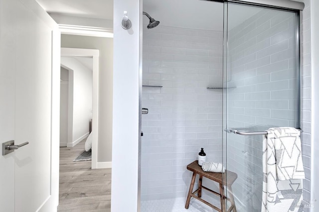 bathroom with tiled shower, baseboards, and wood finished floors