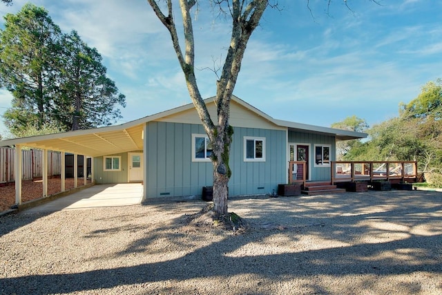 rear view of property featuring gravel driveway, board and batten siding, crawl space, a deck, and an attached carport