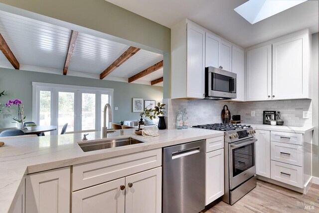 kitchen featuring white cabinets, light wood-type flooring, high end fridge, a kitchen bar, and beamed ceiling