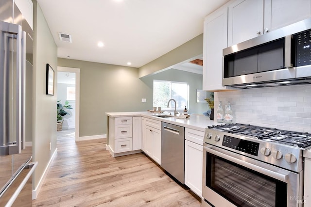 kitchen featuring appliances with stainless steel finishes, a peninsula, a sink, white cabinetry, and backsplash