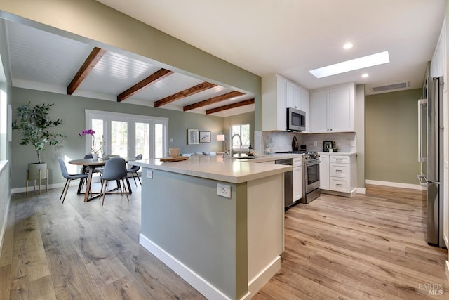 kitchen featuring a skylight, decorative backsplash, appliances with stainless steel finishes, white cabinetry, and a sink