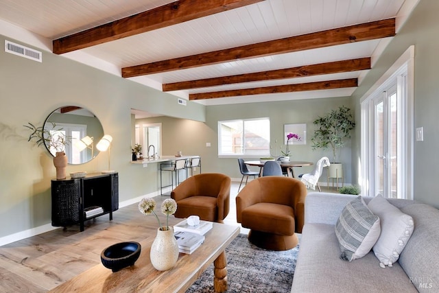 living area with light wood finished floors, baseboards, visible vents, and beamed ceiling