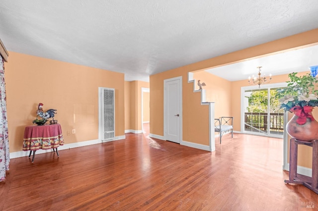 unfurnished living room featuring an inviting chandelier, a textured ceiling, and hardwood / wood-style flooring