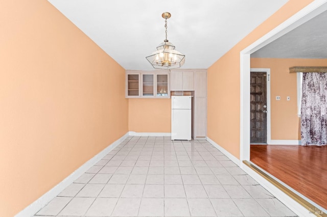 empty room featuring baseboards, a notable chandelier, and light tile patterned flooring