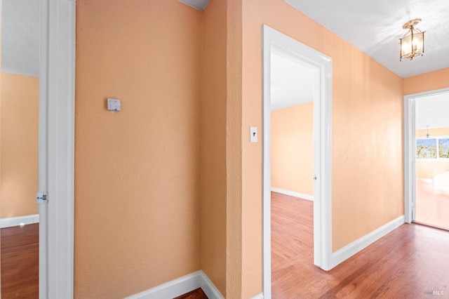 corridor with hardwood / wood-style floors and a notable chandelier