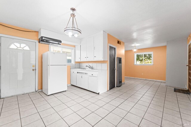 kitchen with sink, white refrigerator, decorative light fixtures, white cabinets, and light tile patterned flooring