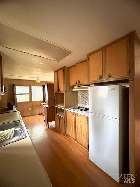 kitchen with backsplash, white appliances, wooden walls, sink, and light hardwood / wood-style floors