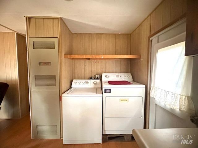 laundry area with wood walls, washer and clothes dryer, and light wood-type flooring