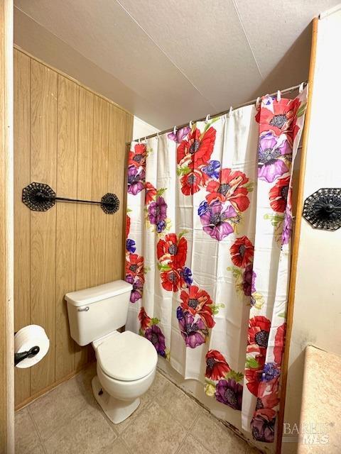 bathroom with a shower with curtain, toilet, a textured ceiling, and wooden walls