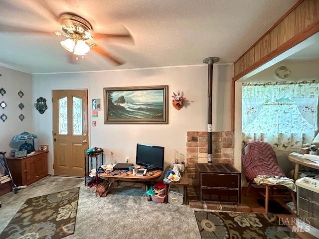 carpeted office with ceiling fan, a wood stove, and a textured ceiling