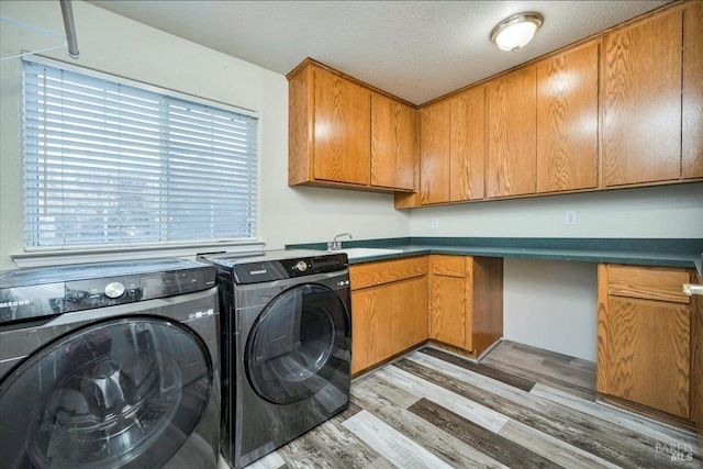 laundry room with cabinets, a textured ceiling, sink, washer and dryer, and light hardwood / wood-style flooring