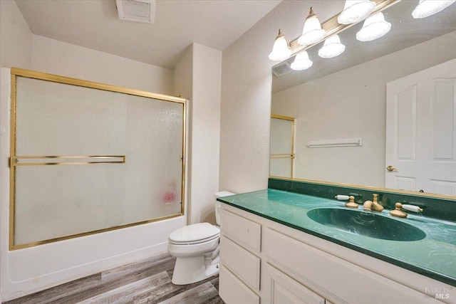 full bathroom with hardwood / wood-style flooring, toilet, combined bath / shower with glass door, and vanity