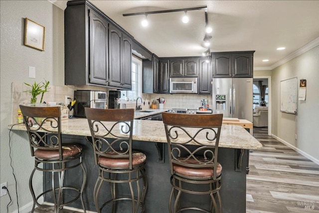 kitchen with sink, crown molding, decorative backsplash, light stone counters, and stainless steel appliances