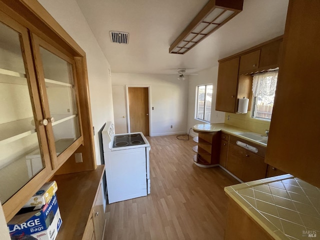 kitchen with ceiling fan, sink, washer / clothes dryer, tile countertops, and light wood-type flooring