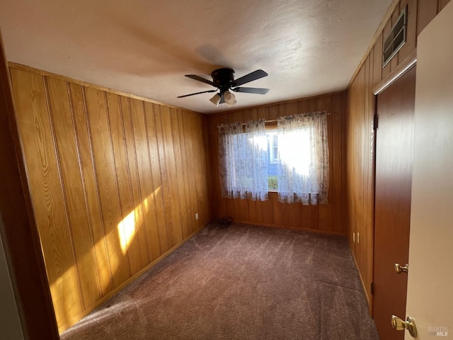 carpeted spare room featuring wood walls, a ceiling fan, and visible vents