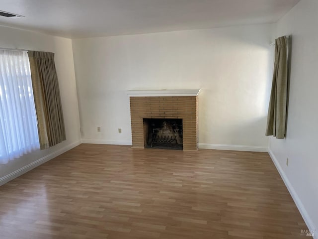 unfurnished living room featuring a brick fireplace, baseboards, visible vents, and wood finished floors