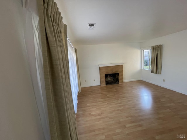 unfurnished living room with a brick fireplace, baseboards, light wood-type flooring, and visible vents