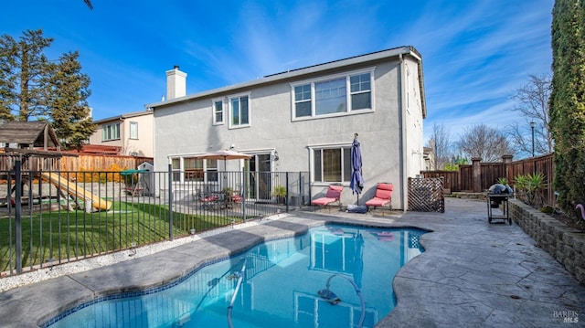 back of house with a yard, a playground, a patio, and a fenced in pool