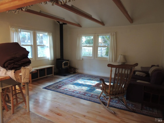 sitting room featuring vaulted ceiling with beams, a healthy amount of sunlight, light wood-type flooring, and a wood stove