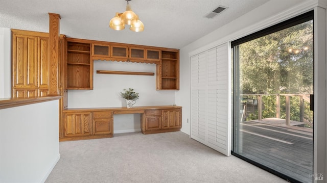 unfurnished office with light carpet, plenty of natural light, built in desk, and a textured ceiling