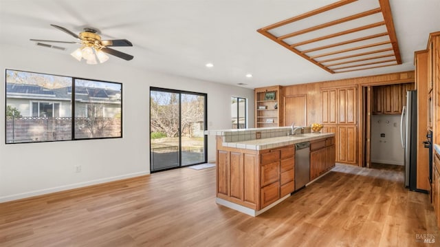 kitchen with tile counters, ceiling fan, appliances with stainless steel finishes, and light hardwood / wood-style flooring